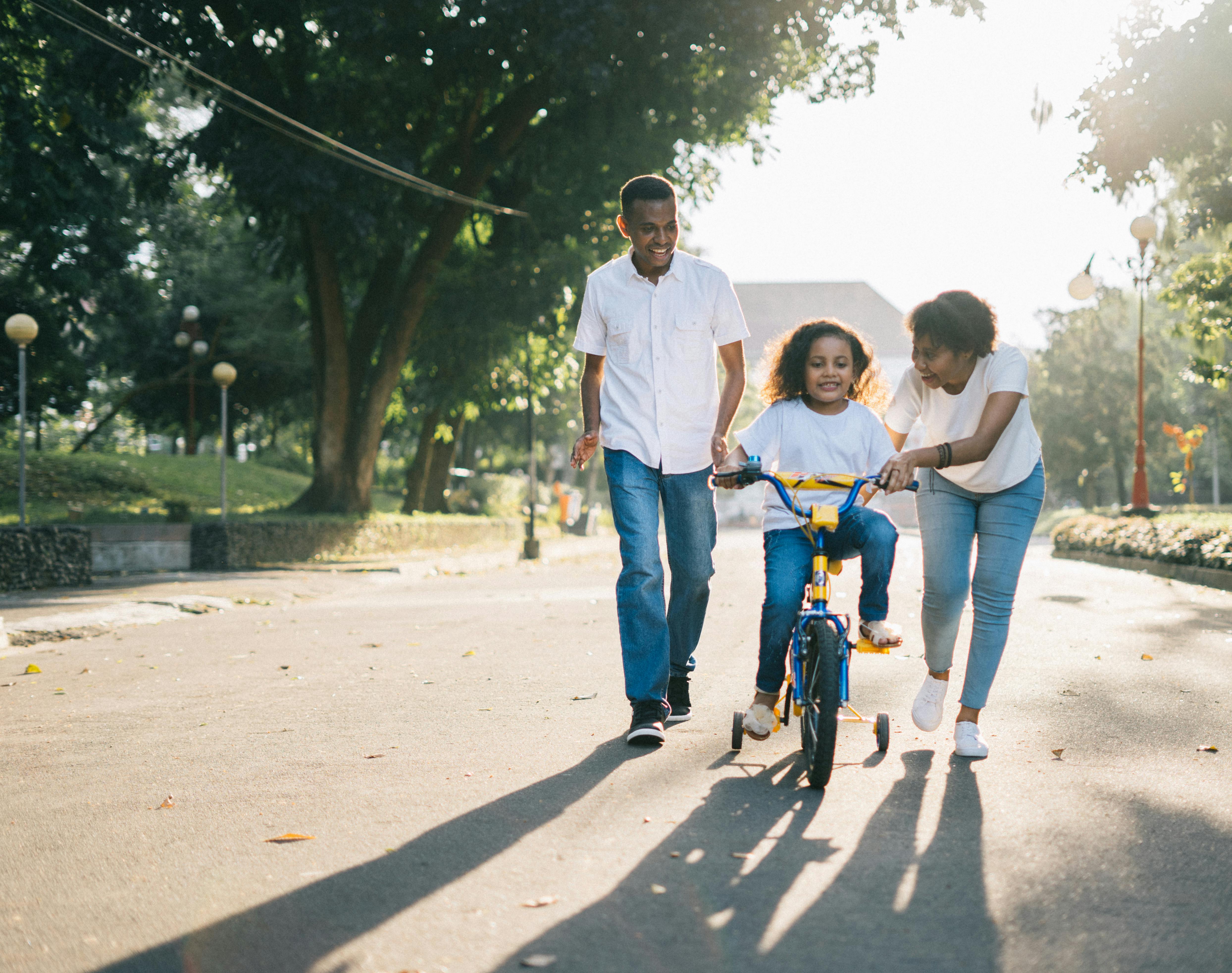 A family of three is walking together in a park with a child on a bicycle.